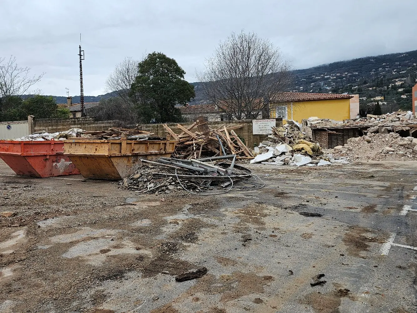 Chantier de démolition avec gravats, conteneurs à déchets et villa en ruines en arrière-plan
