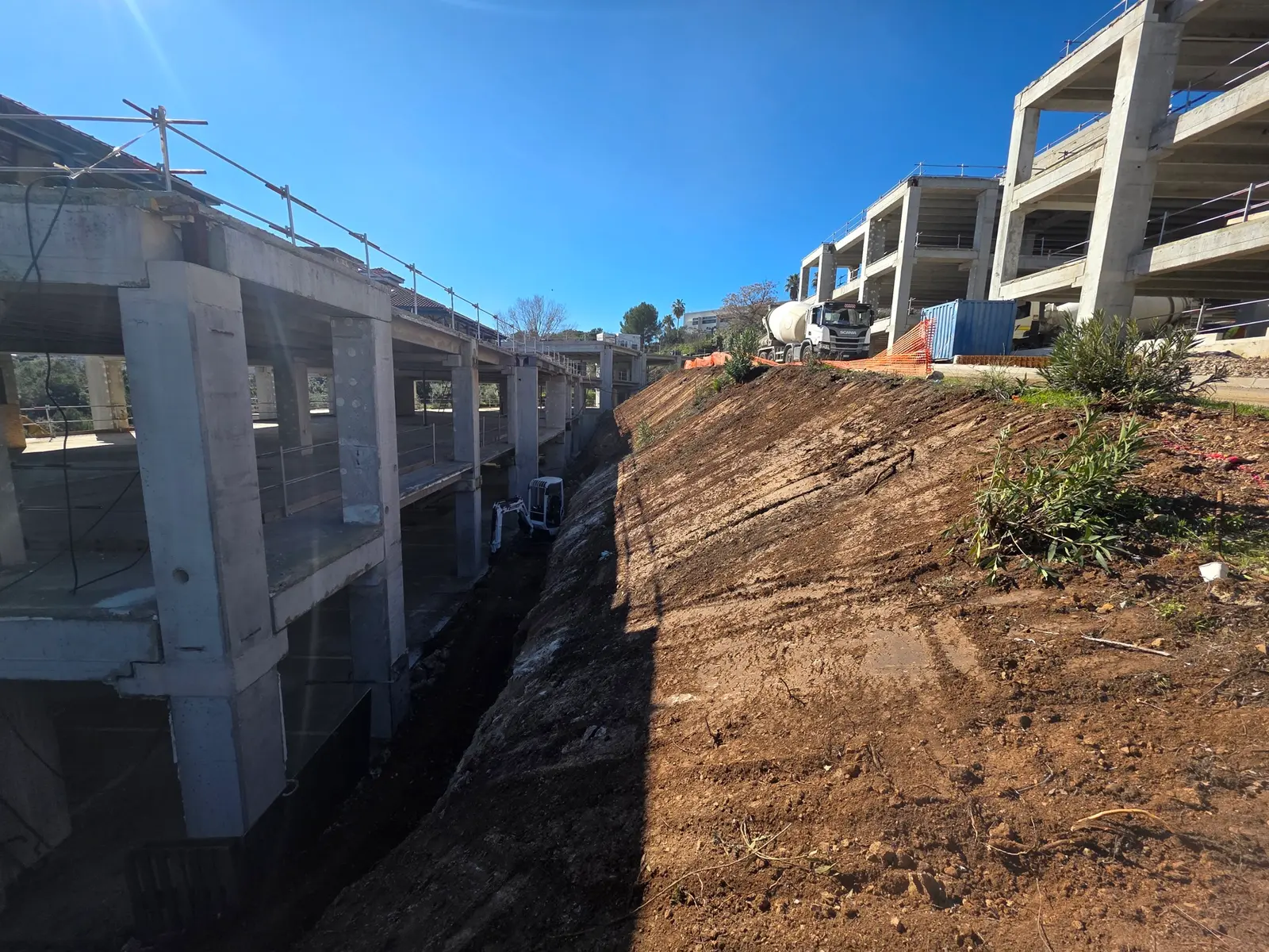 Terrassement d'un talus avec mini-pelle CAT pour agrandissement de surlargeur, chantier en cours près de structures en béton.